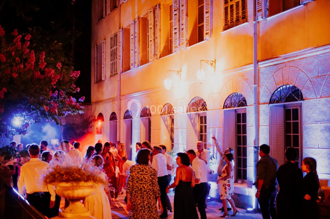 Groupe de personnes dansant en soirée devant un bâtiment éclairé par des lumières colorées.