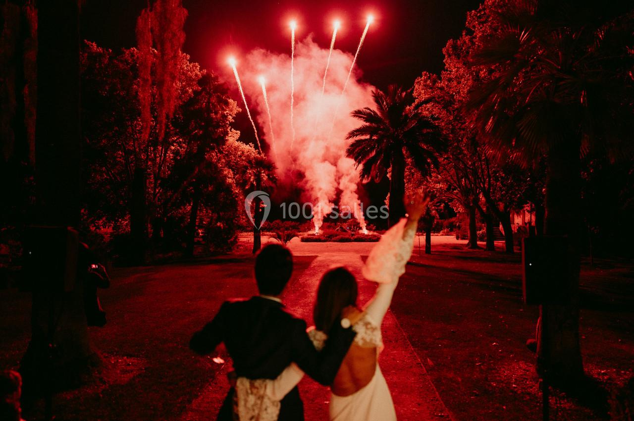 Un couple de dos regarde un feu d'artifice rouge éclatant dans un jardin la nuit.