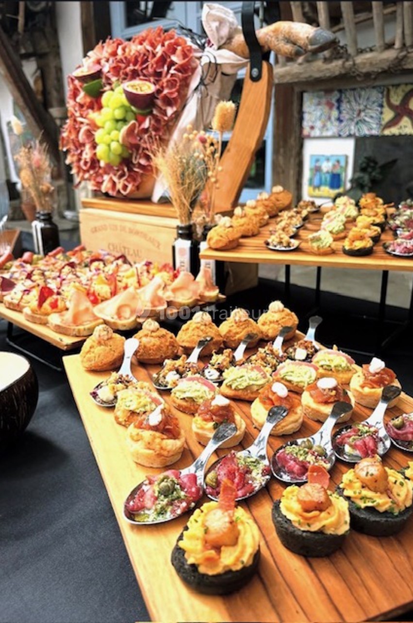 Plateau de bouchées apéritives variées, incluant cuillères garnies, mini-tartelettes et charcuterie, sur une table en bois.