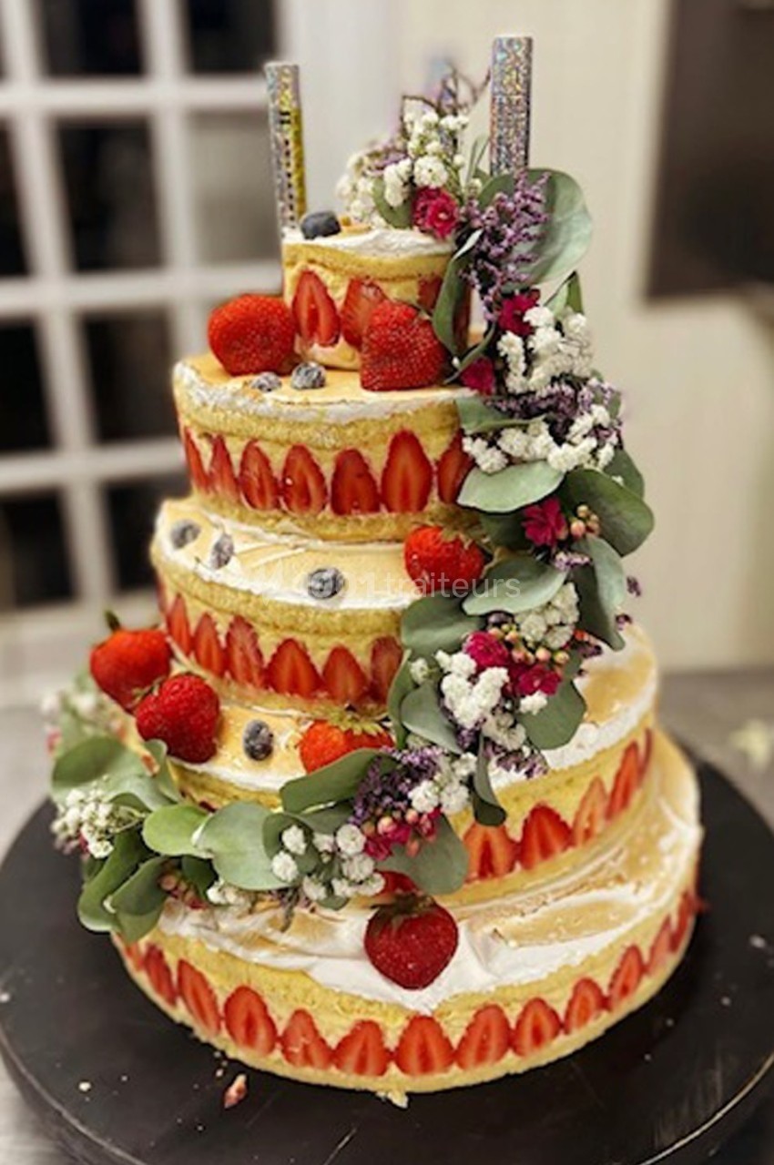Gâteau de mariage à étages décoré de fraises, myrtilles, fleurs fraîches et bougies scintillantes.