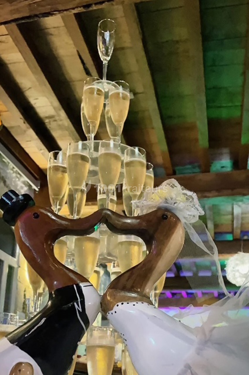 Deux sculptures de cygnes en bois formant un cœur devant une pyramide de coupes de champagne sous un plafond en bois.