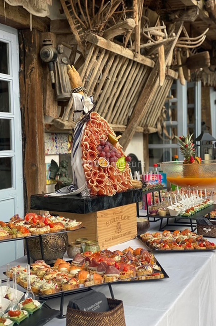 Plateau de charcuterie et fruits décoratif entouré de divers amuse-bouches sur une table lors d'un buffet en extérieur.