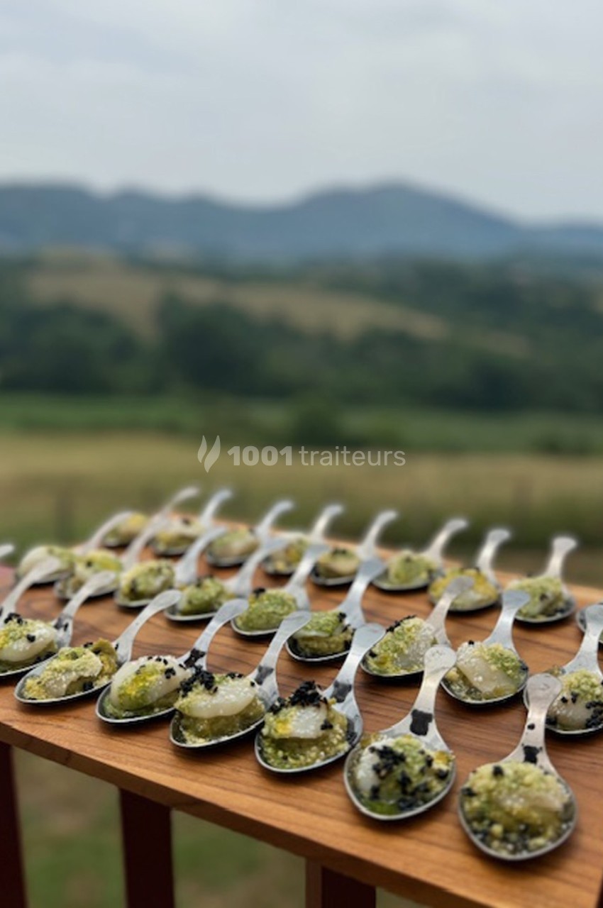 Cuillères garnies de préparations culinaires colorées, disposées sur une planche en bois avec un paysage vallonné en arrière…