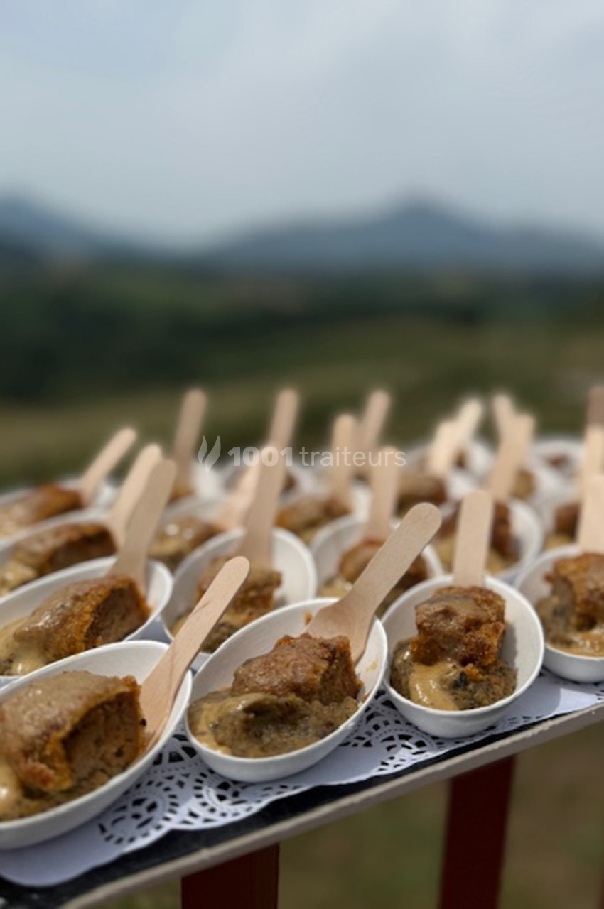 Portions individuelles de gâteau servies dans des cuillères blanches avec une sauce, présentées sur un plateau en extérieur.