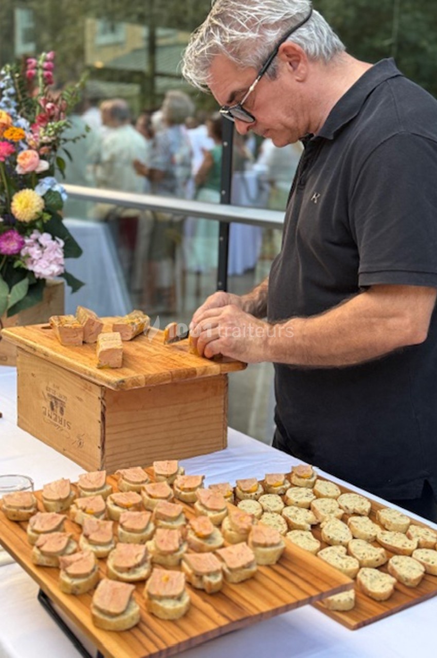 Un homme prépare des toasts au foie gras sur une table garnie de fleurs et de plateaux en bois lors d'un événement en…