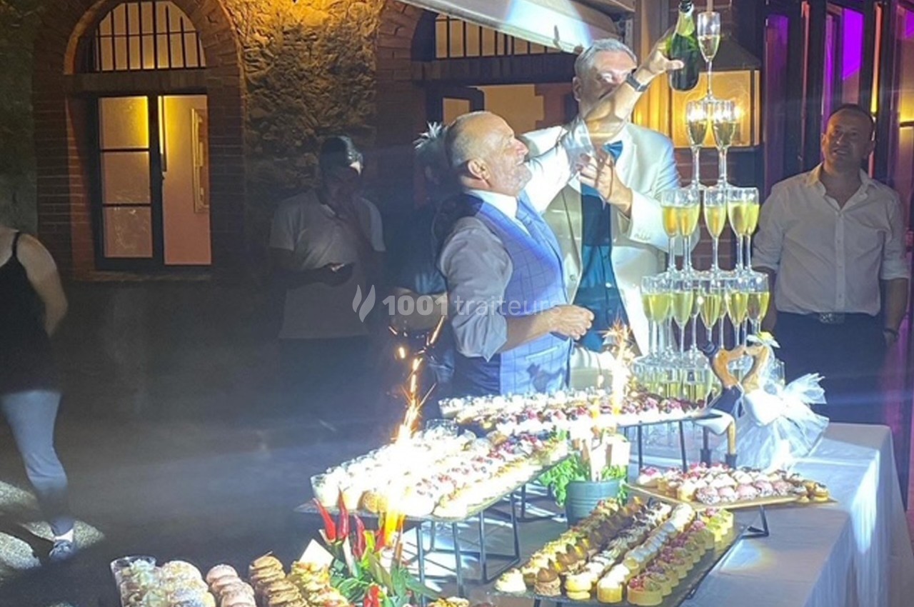 Des invités remplissent une pyramide de coupes de champagne lors d'une réception en soirée, entourés de desserts.