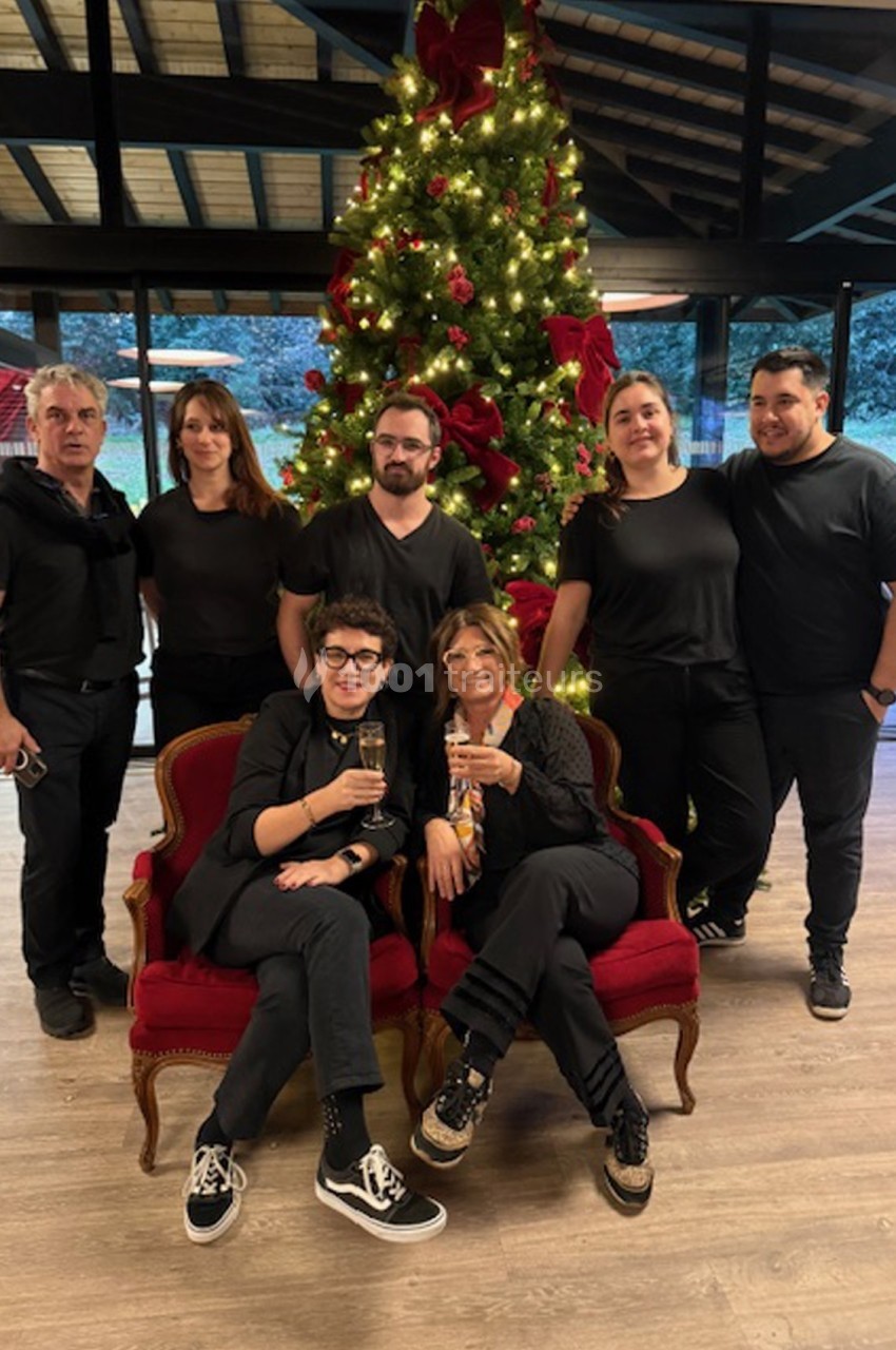 Un groupe de personnes pose devant un sapin de Noël décoré, deux d'entre elles assises sur des fauteuils rouges.