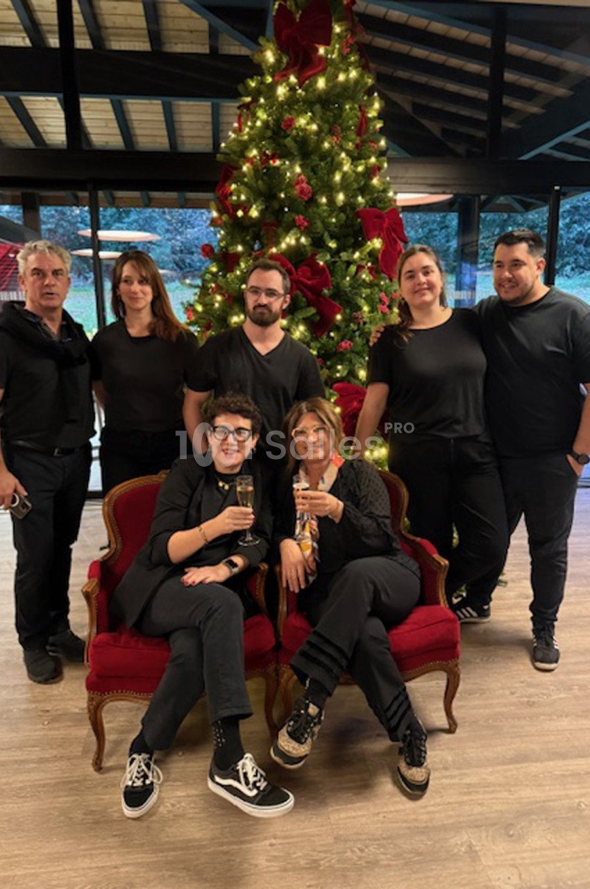 Un groupe de personnes pose devant un sapin de Noël décoré, deux d'entre elles assises sur des fauteuils rouges.