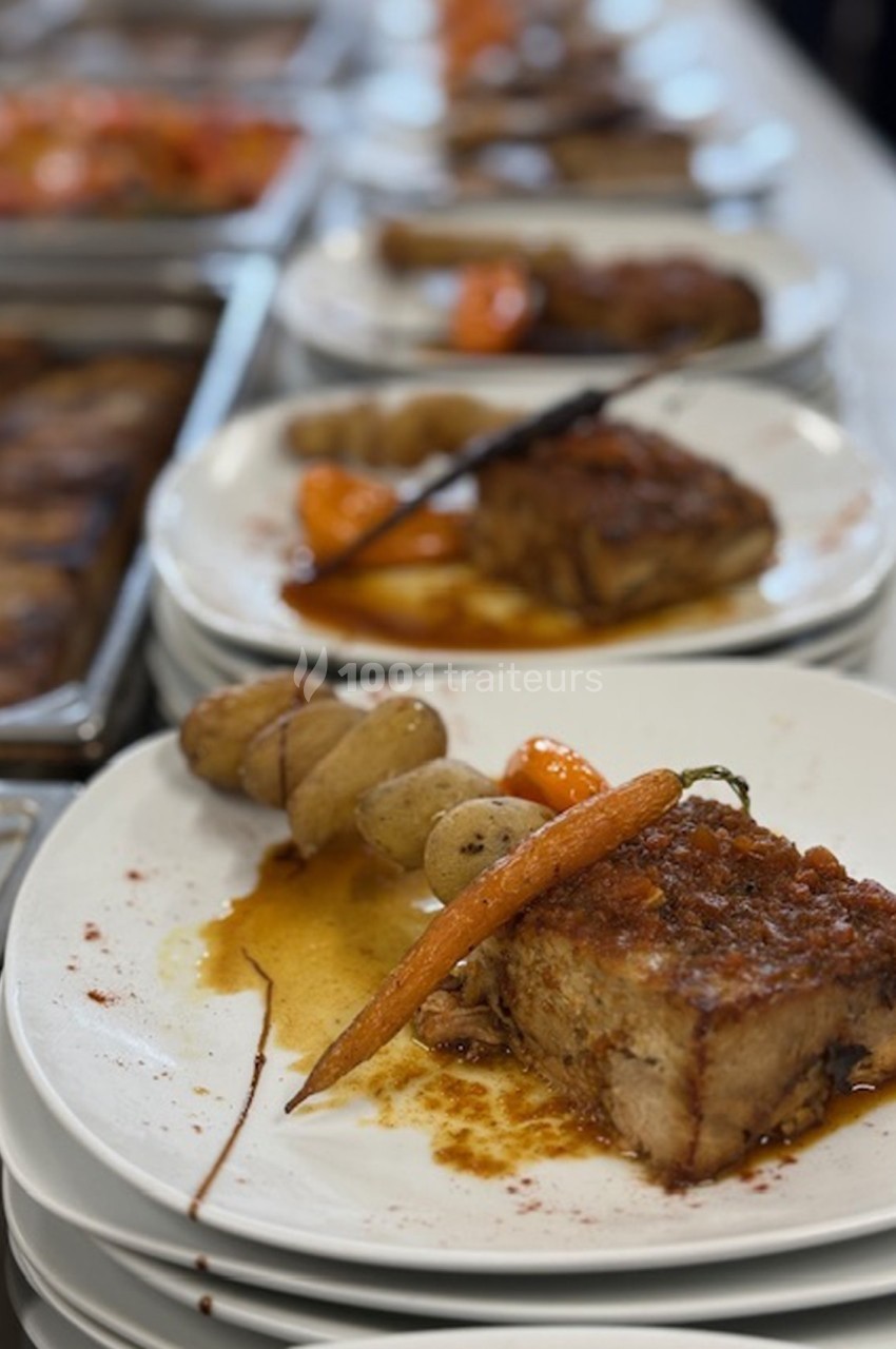 Assiette de viande braisée accompagnée de carottes glacées et pommes de terre, servie sur une table de buffet.