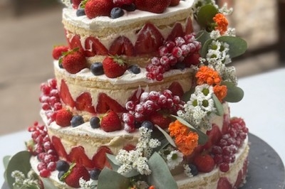 Gâteau à plusieurs étages décoré de fraises, myrtilles et roses rouges, avec des pailles en décoration.