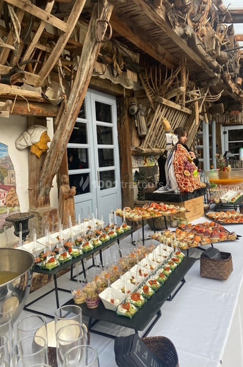 Buffet varié avec verrines, brochettes et plats disposés sur une table blanche dans un décor rustique en bois.