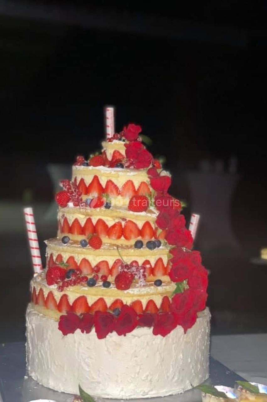 Gâteau à plusieurs étages décoré de fraises, myrtilles et roses rouges, avec des pailles en décoration.