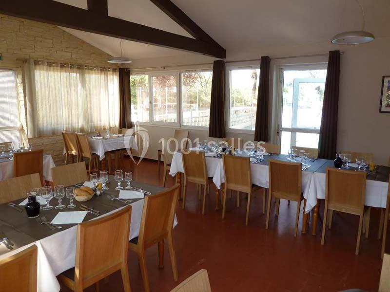 Salle de restaurant lumineuse avec tables dressées, nappes blanches et chaises en bois, vue sur l'extérieur.