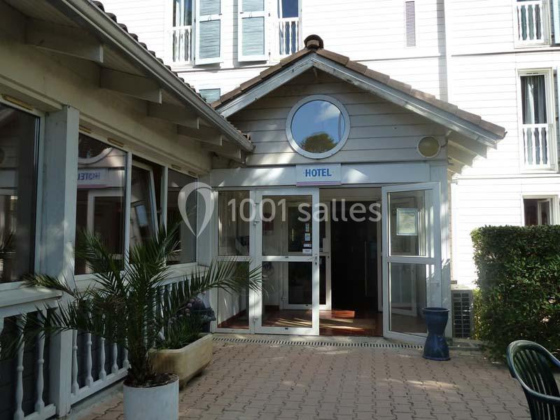 Entrée principale d'un hôtel avec façade en bois clair, porte vitrée et plantes décoratives sur le devant.