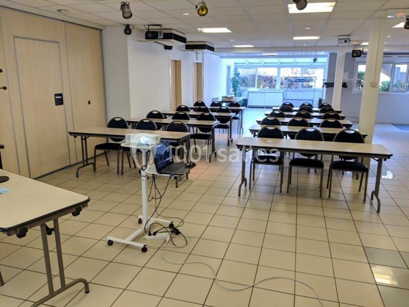 Salle de réunion lumineuse avec des tables, des chaises alignées et un projecteur installé au premier plan.