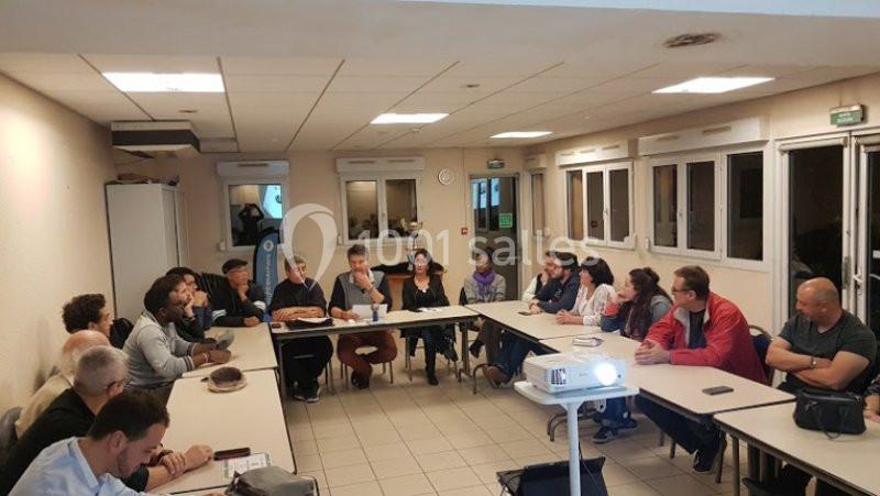 Réunion de personnes assises autour de tables en U dans une salle équipée d'un vidéoprojecteur.