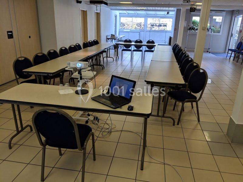 Salle de réunion avec tables disposées en U, un vidéoprojecteur et un ordinateur portable installés au premier plan.