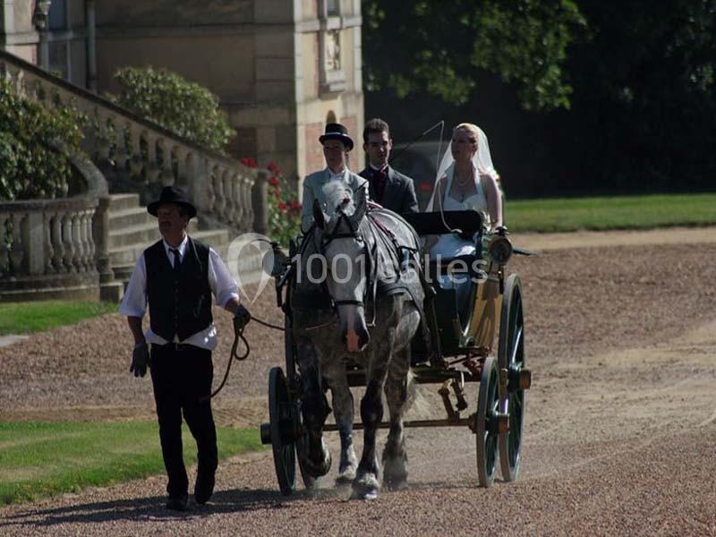 Un couple en tenue de mariage est transporté dans une calèche tirée par un cheval, guidée par un cocher.