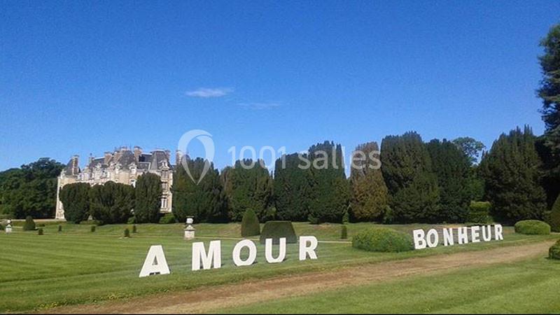 Lettres géantes formant ’AMOUR’ et ’BONHEUR’ dans un parc verdoyant avec un château en arrière-plan.