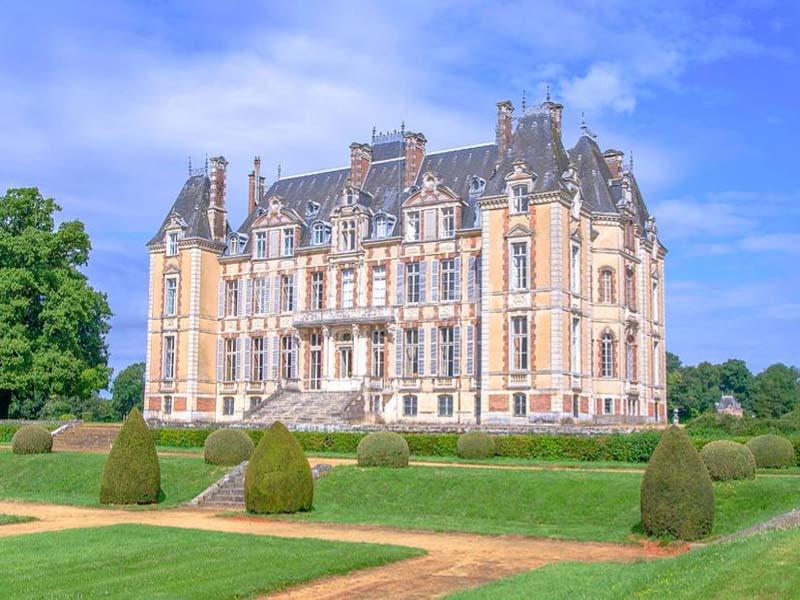 Château historique entouré de jardins bien entretenus, avec ciel bleu en arrière-plan.