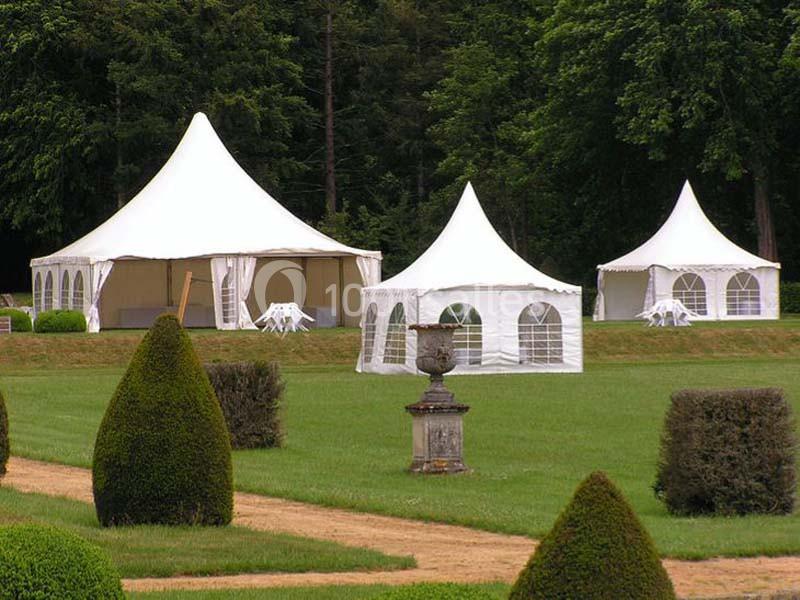 Trois tentes blanches installées sur une pelouse entourée d'arbres, avec des chaises et tables à l'intérieur.