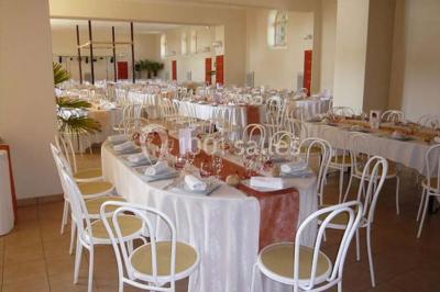 Salle de réception décorée avec des tables rondes, nappes blanches, chaises assorties et ornements dorés.