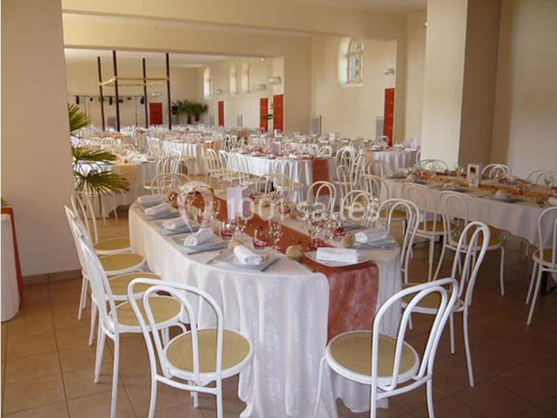 Salle de réception aménagée avec des tables dressées, nappes blanches et chaises blanches, prête pour un événement.