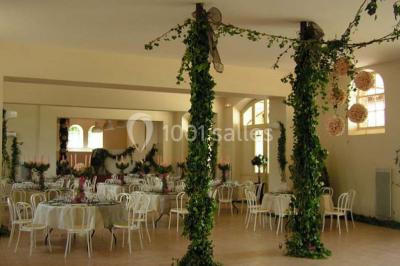 Salle de réception décorée avec des tables rondes, nappes blanches, chaises assorties et ornements dorés.
