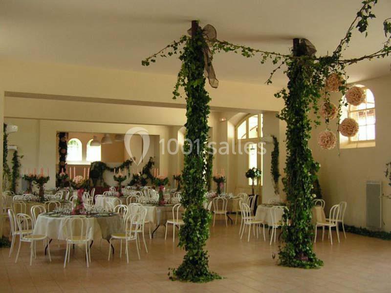 Salle de réception décorée avec des guirlandes de lierre, des tables rondes dressées et des chaises blanches.
