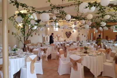 Salle de réception décorée avec des tables rondes, nappes blanches, chaises assorties et ornements dorés.