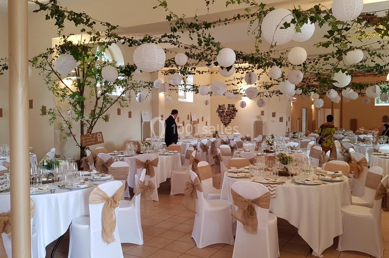 Salle de réception décorée avec des guirlandes végétales, lanternes blanches suspendues et tables dressées pour un événement.