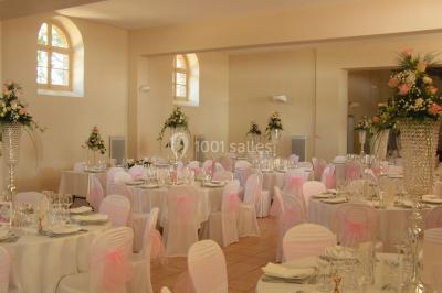 Salle de réception décorée avec des tables rondes, nappes blanches, chaises assorties et ornements dorés.