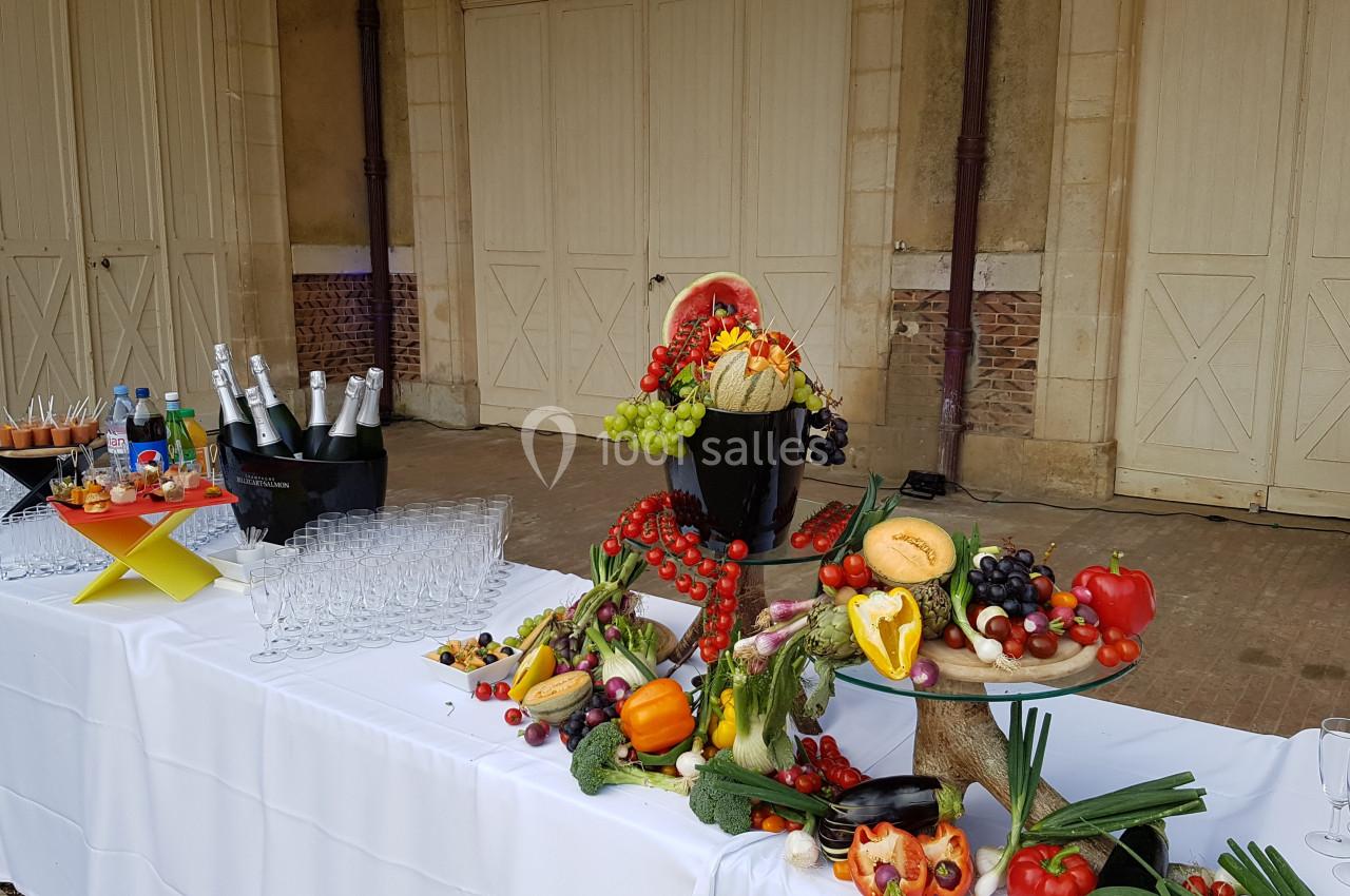 Buffet extérieur avec fruits variés, bouteilles de champagne, verres et décorations sur des tables blanches.