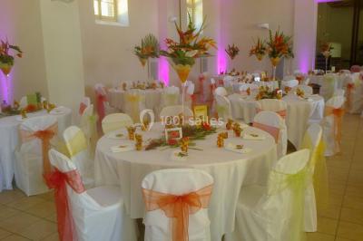 Salle de réception décorée avec des tables rondes, nappes blanches, chaises assorties et ornements dorés.