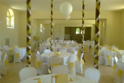 Salle de réception décorée avec des tables rondes, nappes blanches, chaises assorties et ornements dorés.