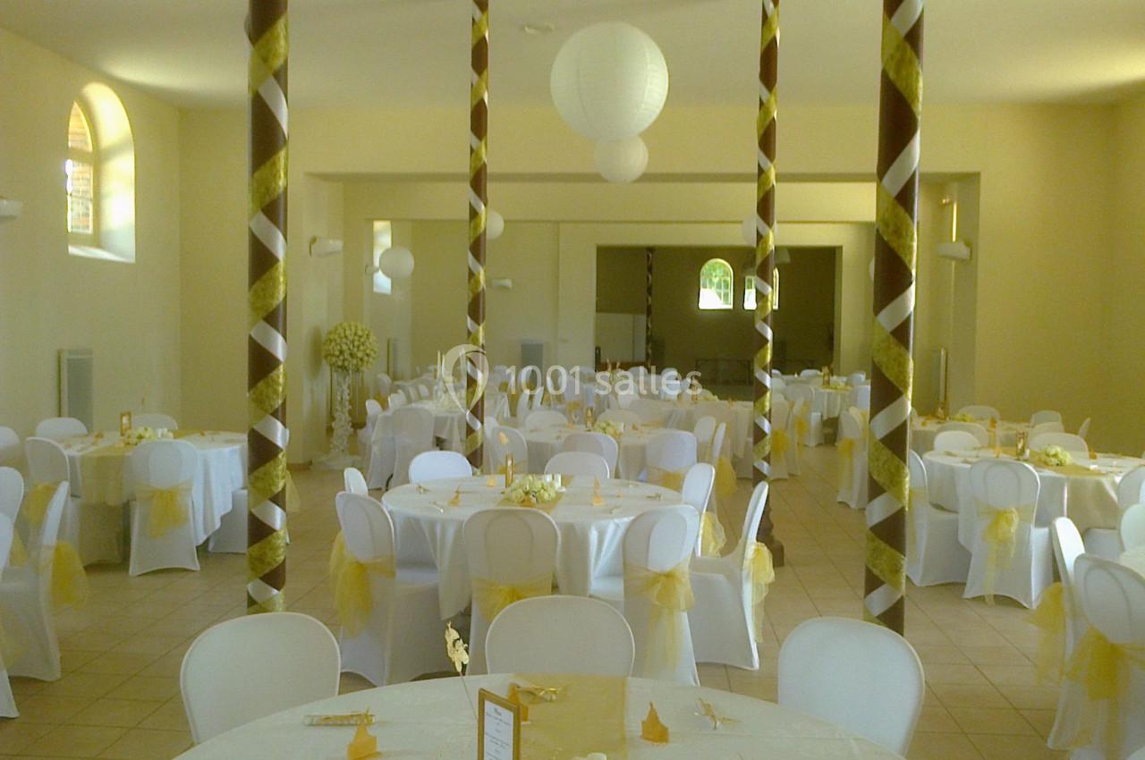 Salle de réception décorée avec des tables rondes, nappes blanches, chaises assorties et ornements dorés.