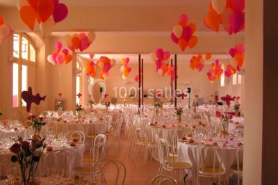 Salle de réception décorée avec des tables rondes, nappes blanches, chaises assorties et ornements dorés.