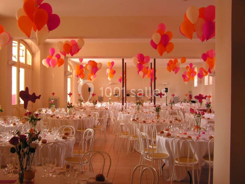 Salle de réception décorée avec des ballons colorés et des tables dressées pour un événement festif.