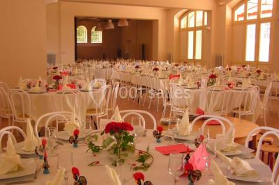 Salle de réception décorée avec des tables rondes, nappes blanches, chaises assorties et ornements dorés.