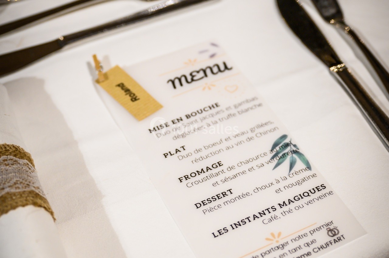 Menu imprimé posé sur une table dressée avec des couverts, une serviette roulée et un verre.