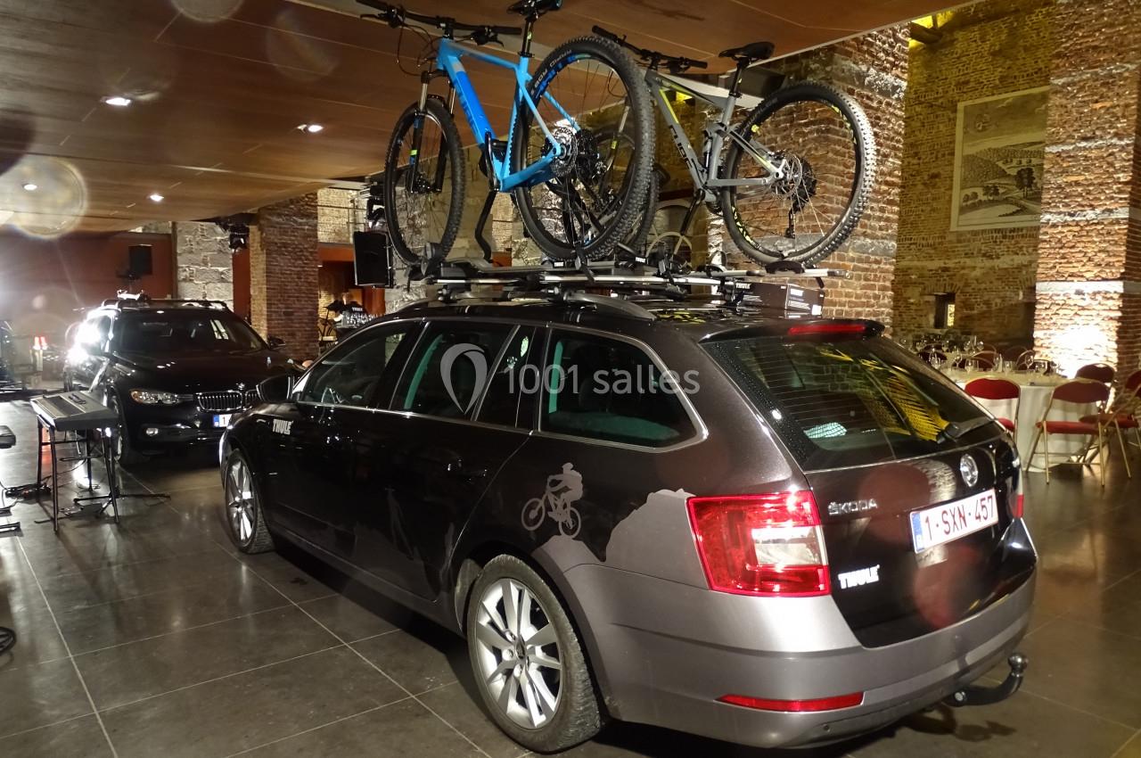 Voiture noire avec deux vélos fixés sur un porte-vélos de toit, stationnée dans un espace intérieur en briques.