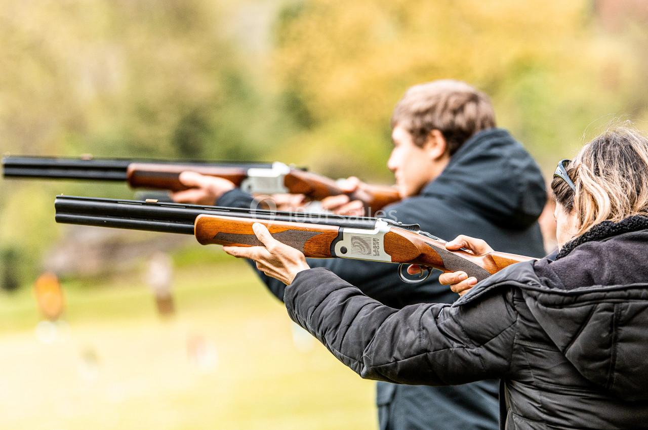 Personnes tenant des fusils de chasse et visant une cible en extérieur, dans un cadre naturel.