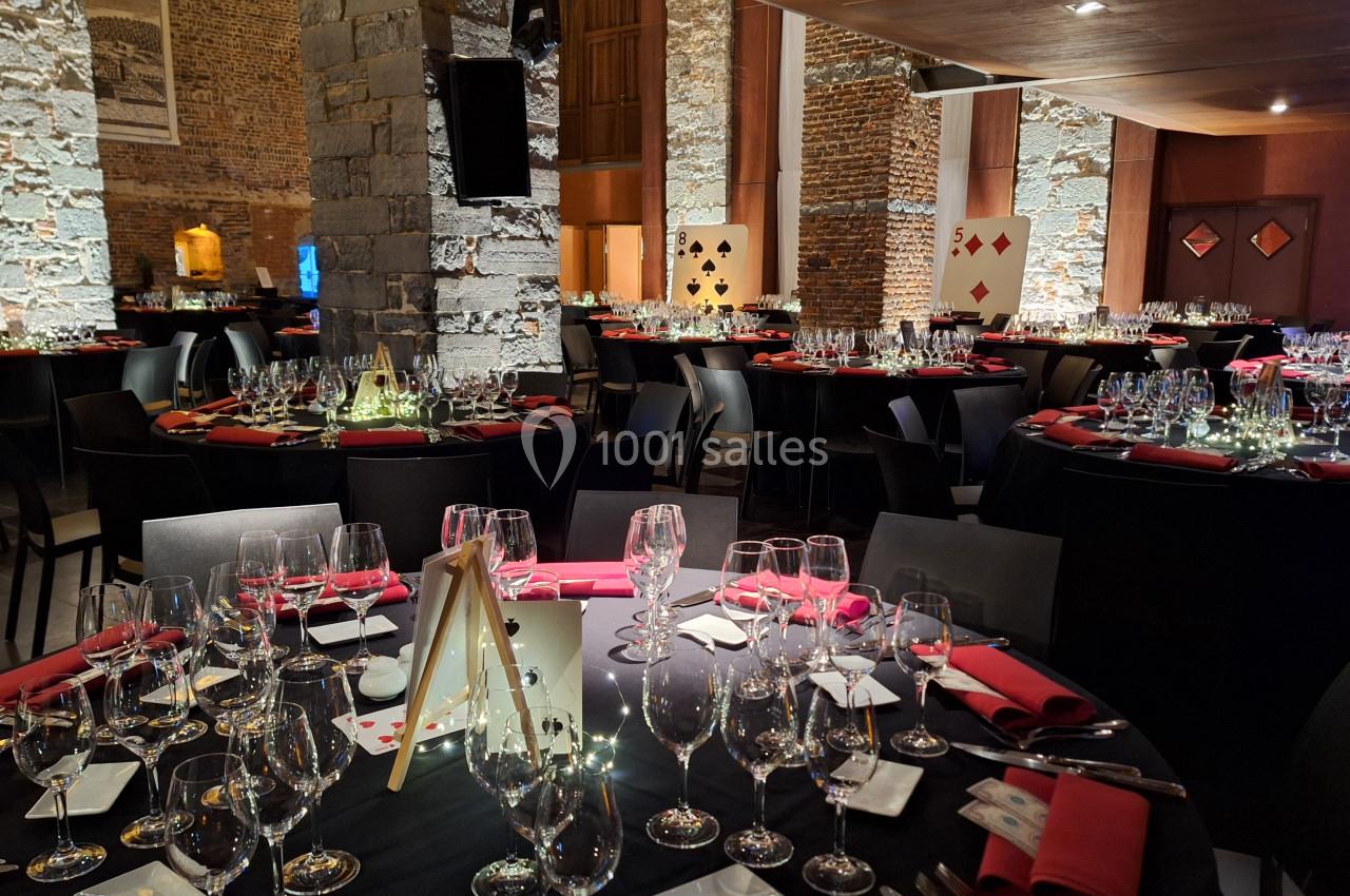 Salle de réception élégante avec tables rondes dressées, nappes noires, serviettes rouges et décorations sur le thème des…