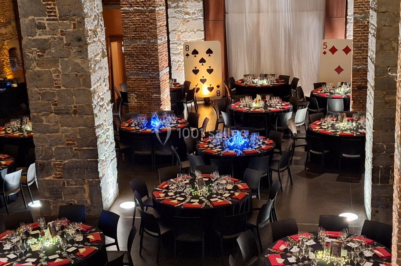 Salle de réception décorée sur le thème des cartes, avec des tables rondes dressées et éclairages colorés.