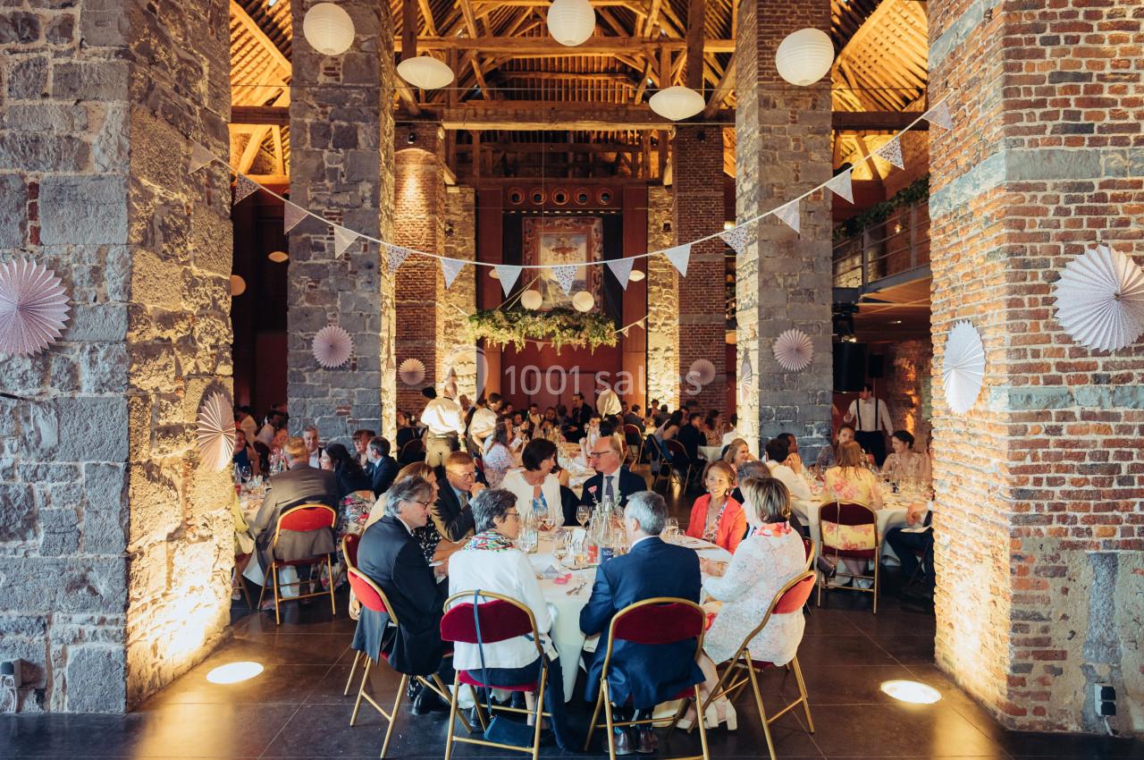 Salle en pierre et briques avec des invités assis à des tables rondes décorées pour un événement festif.