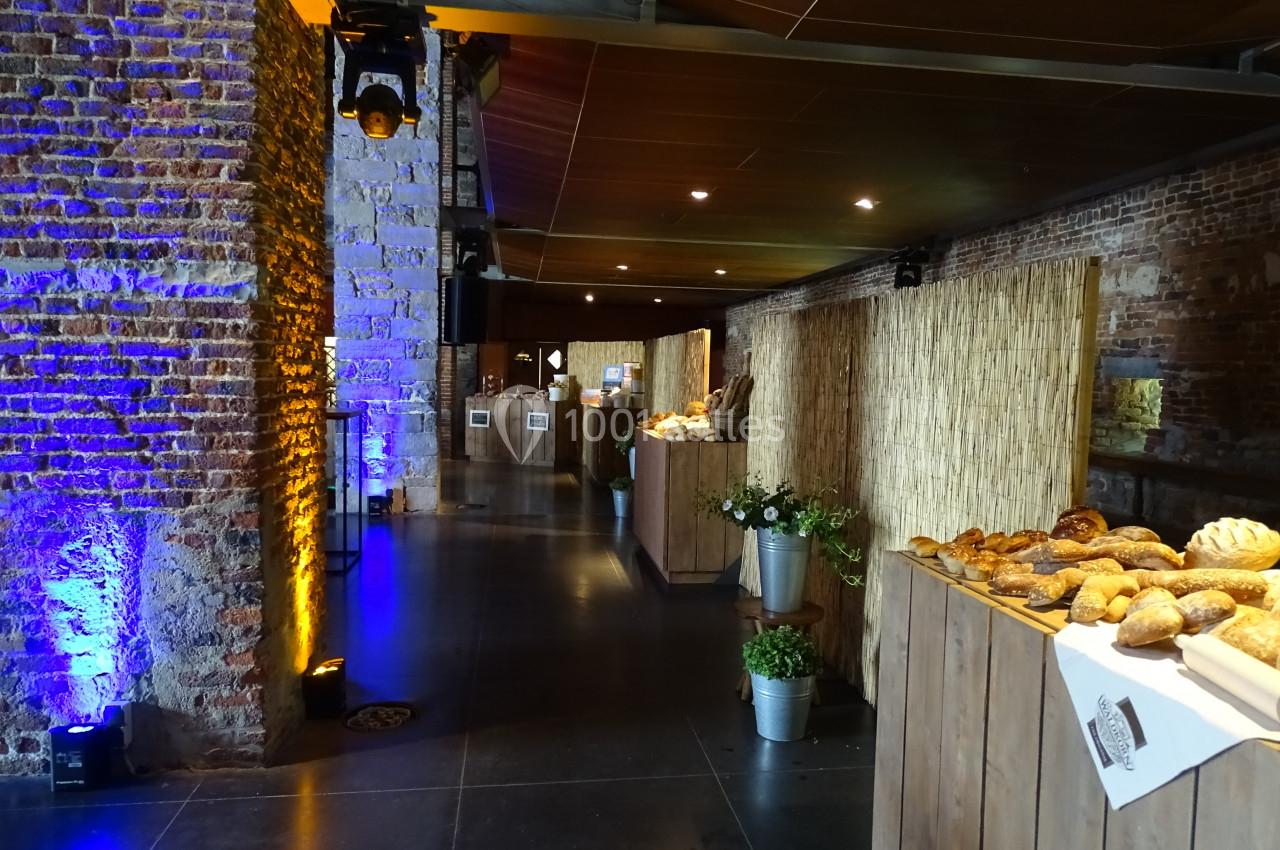 Salle avec murs en briques, éclairage tamisé, tables en bois garnies de pains et décorations végétales.