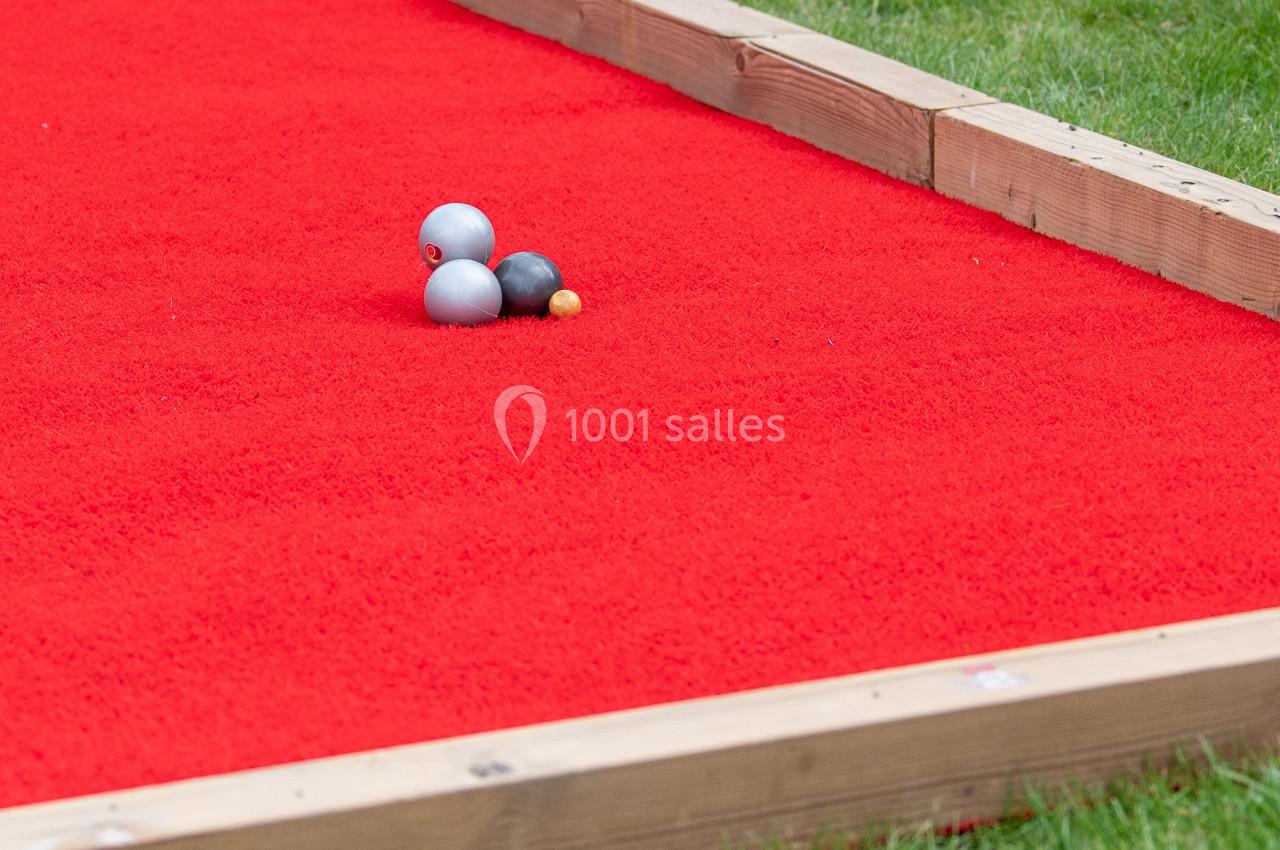 Terrain de pétanque avec tapis rouge, trois boules métalliques et un cochonnet posés au centre.