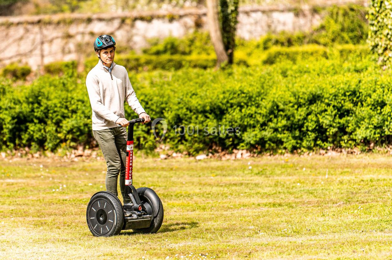 Un homme portant un casque roule sur un gyropode dans un parc verdoyant par une journée ensoleillée.