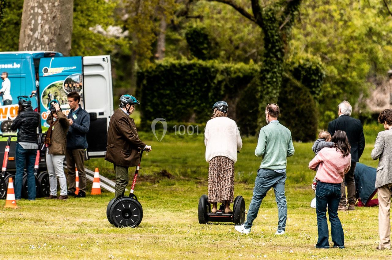Des personnes testent des gyropodes sur une pelouse, avec un camion promotionnel et des cônes en arrière-plan.