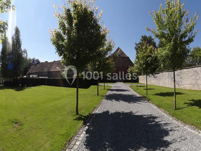 Allée bordée d'arbres menant à un bâtiment en briques rouges, entouré de pelouses et de murs en pierre.